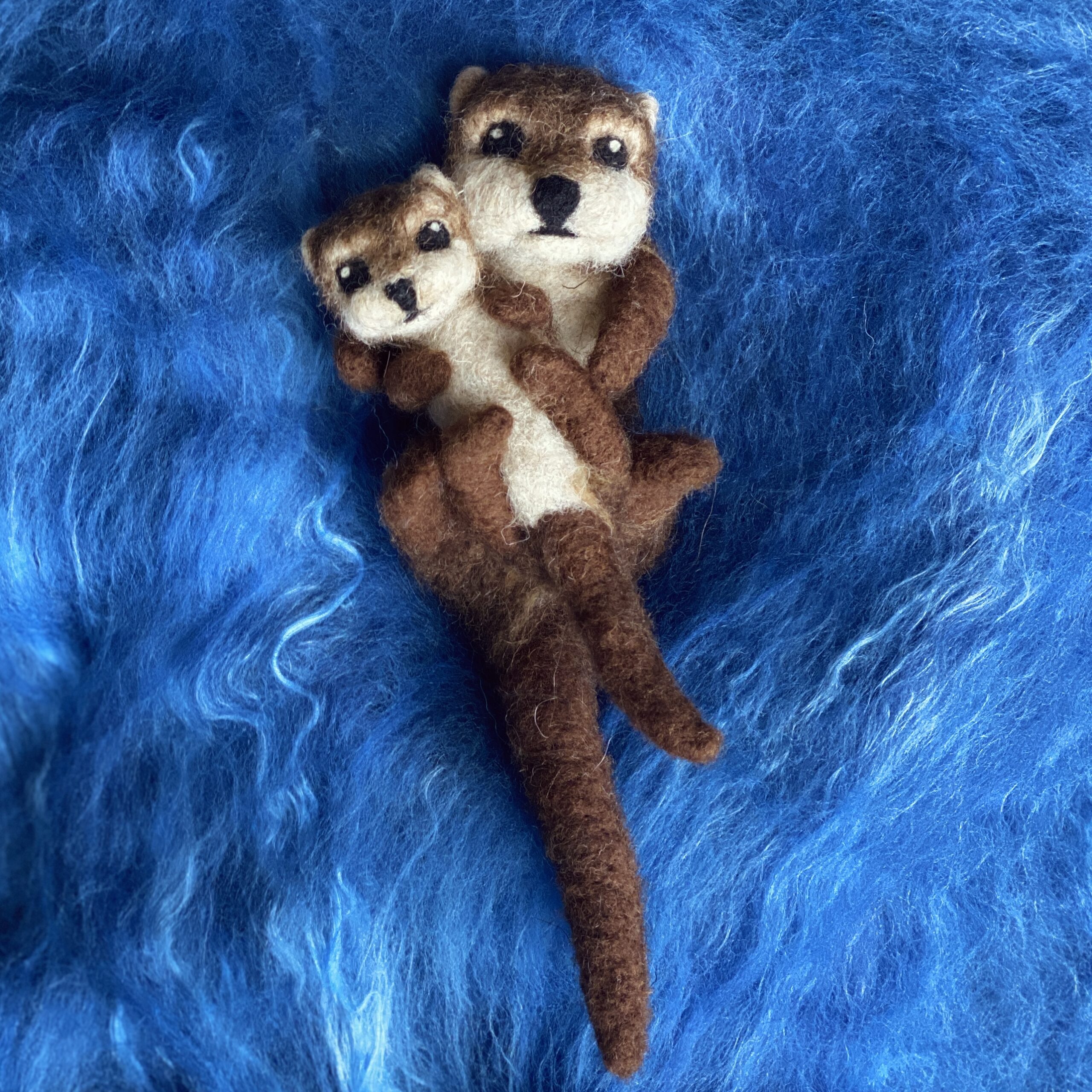 Gefilzte Otter-Figuren, Mutter und Jungtier auf blauem Untergrund