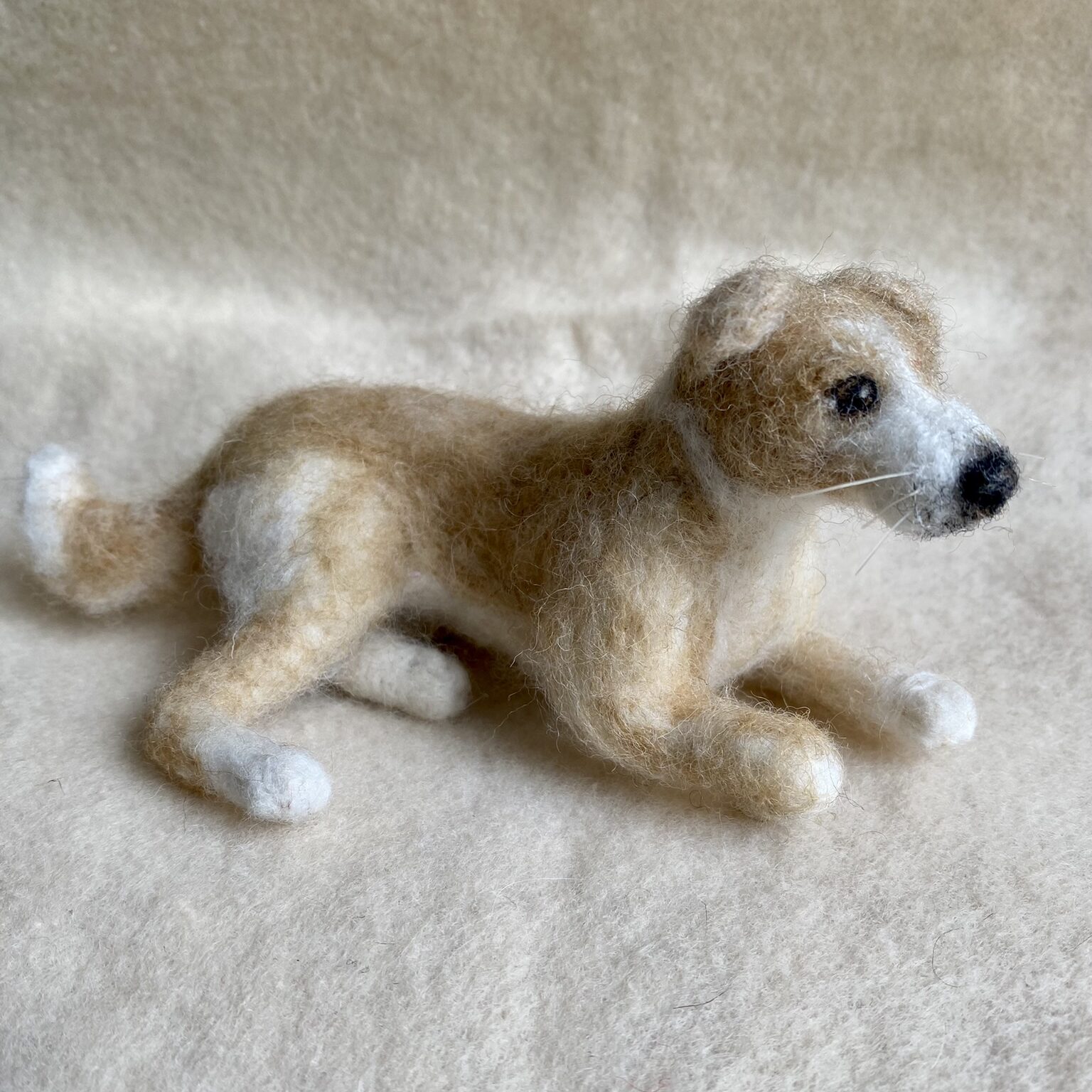 Handgefilzte Hundfigur in hellbraun und weiss, liegend dargestellt